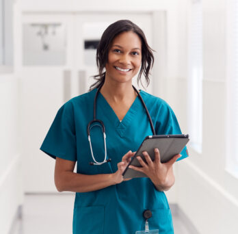 Nurse with a BSN degree smiles and holds up ipad with patient records. 