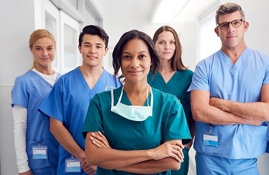 Five nurses standing in a line, smiling at the camera