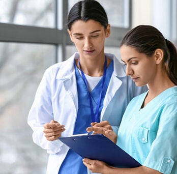 Two nurses reviewing patient notes on a clipboard 